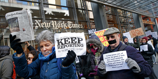 Loading People with taped mouths hold signs and a copy of the New York Times as they show solidarity with the press during a rally in front of The New York Times building