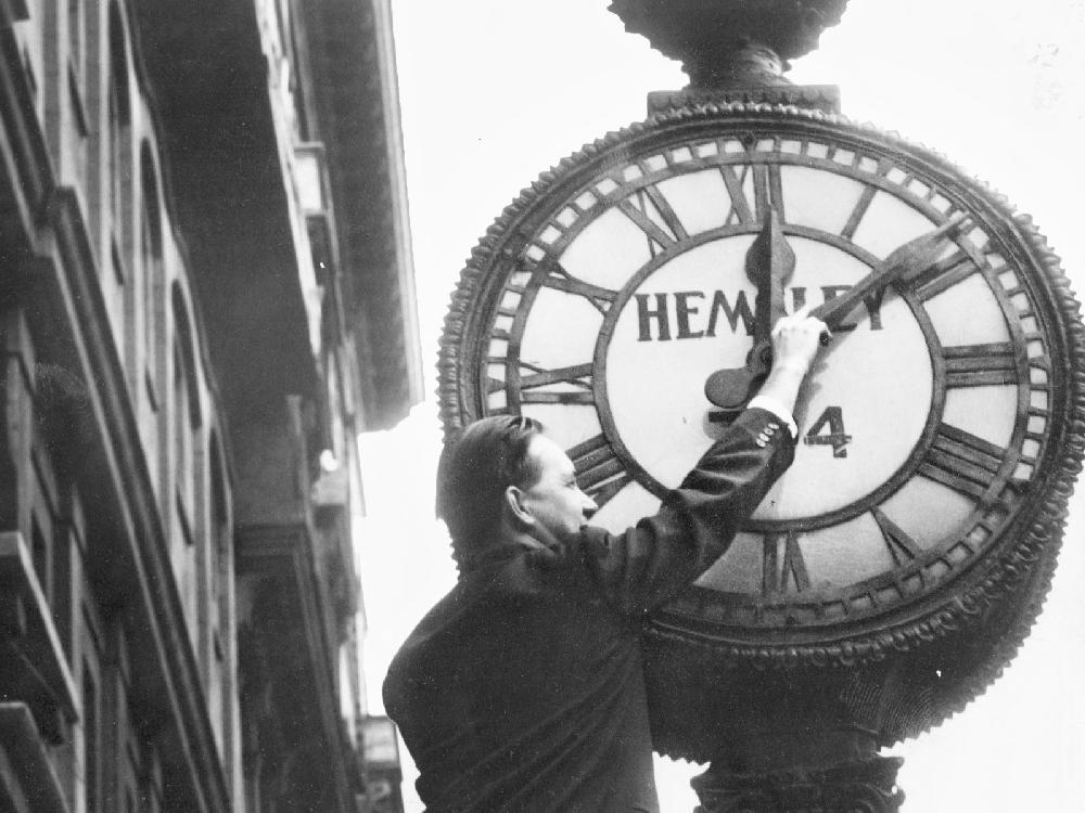 A man moves Hemsley's clock on St Jacques St. ahead an hour for daylight saving time