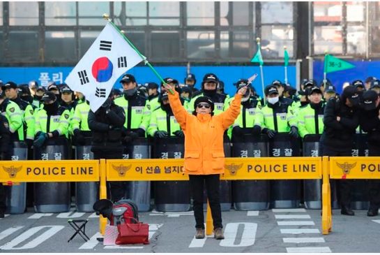 A supporter of impeached South Korean President Park Geun-hye holds a national flag as police officers stand guard near the Constitutional Court in Seoul South Korea Thursday