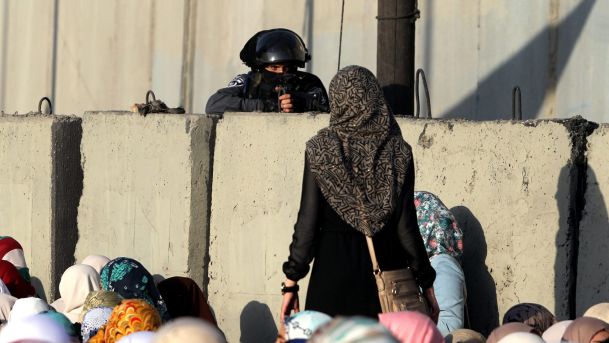 Palestinian woman looks at member of Israeli security forces at Qalandia checkpoint. Palestinians wait to cross from West Bank to Jerusalem for Friday prayers at Al Aqsa Mosque