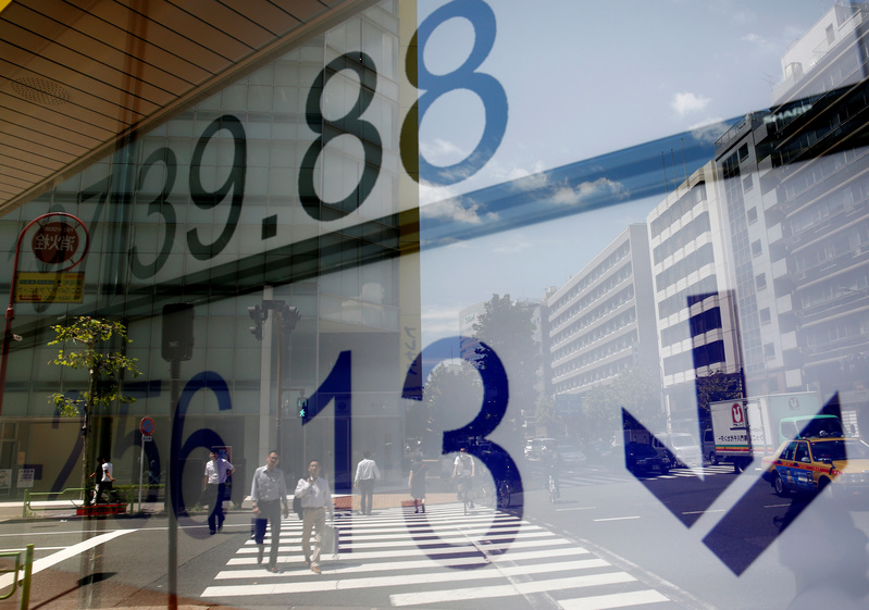 People are reflected on an electronic board showing Japan's Nikkei average outside a brokerage at a business district in Tokyo