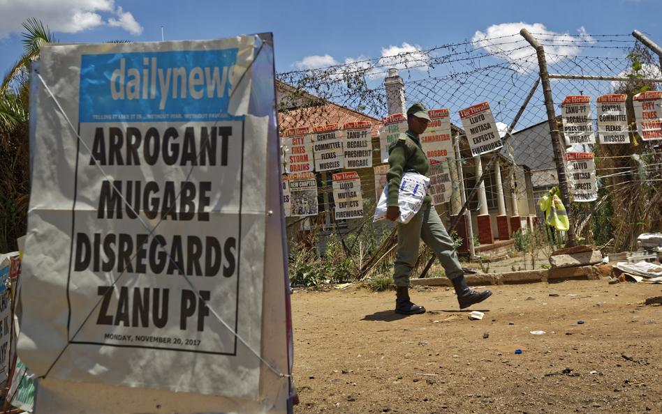 A prison officer walks past a news stand in Harare Zimbabwe Monday Nov. 20 2017. Longtime President Robert Mugabe ignored a midday deadline set by the ruling party to step down or face impeachment proceedings while Zimbabweans stunned by his lack