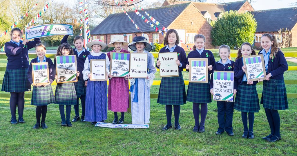 Girls from Sibford Junior School hold Votes for Women signs