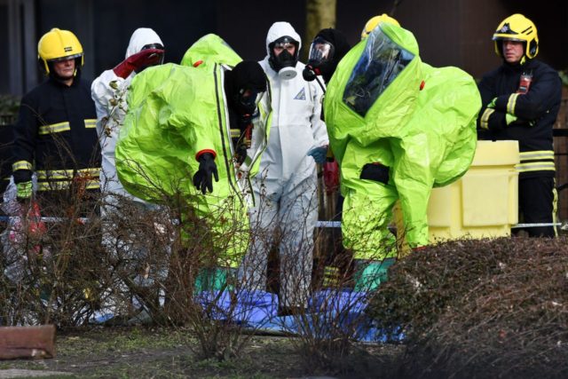 Members of the fire brigade are helped out of their green biohazard suits by colleagues in white protective coveralls after an operation to re-attach the tent over the bench where a man and a woman were found in critical condition sparking a major inciden