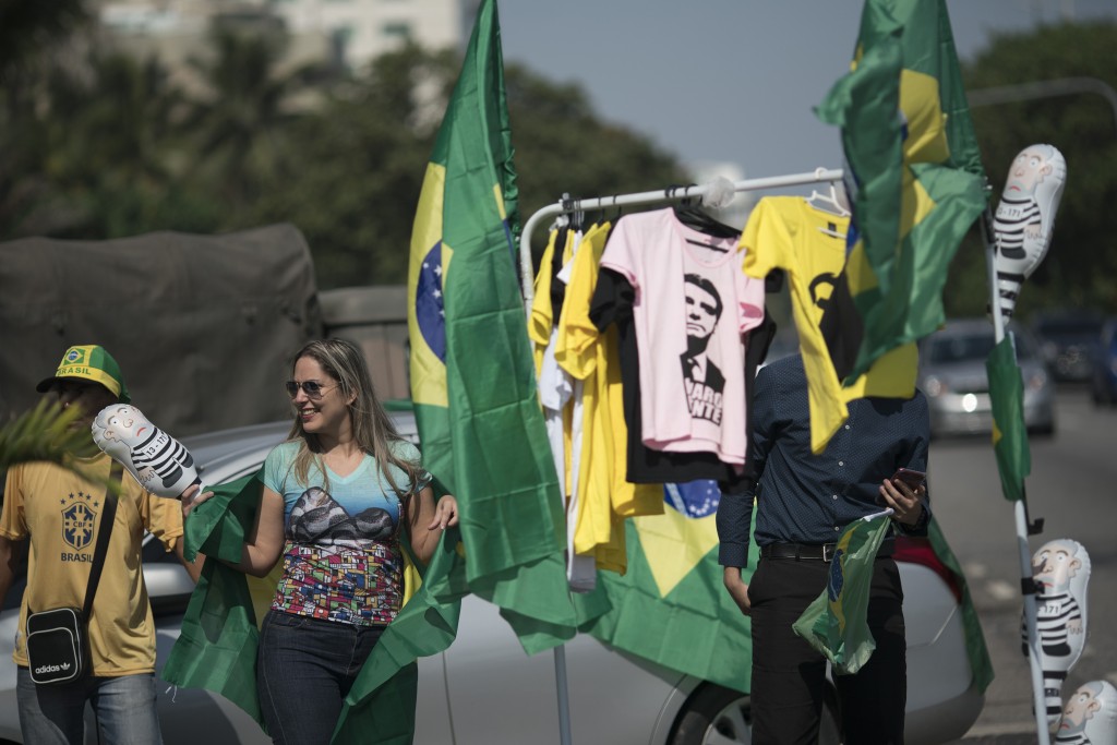 A supporter of presidential candidate Jair Bolsonaro of the Social Liberal Party buys a Brazilian flag being sold in front of the entrance of Bolsona